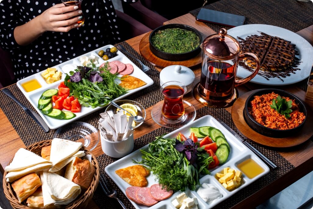 side-view-breakfast-table-served-with-various-food-fried-eggs-sausages-cheese-fresh-salad-dessert-tea@2x
